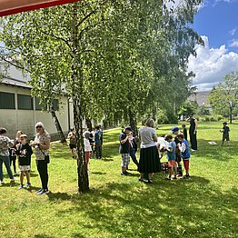 Menschen mit Eis stehen in Gruppen auf einer großen Wiese im Sonnenschein.