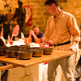 Ein Mann in mittelalterlicher Kleidung serviert Suppe in Schüsseln.